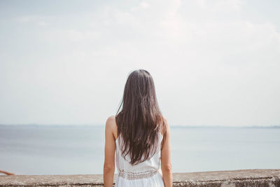 Rear view of woman standing by retaining wall against sky