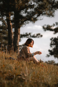 Side view of young woman sitting on field