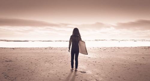 Rear view of woman standing at beach against sky