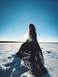 Woman sitting on shore against sea against clear sky