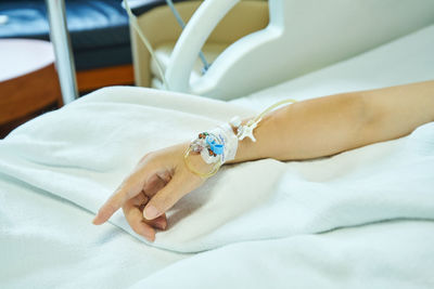 Cropped hand of woman with iv drip on bed in hospital