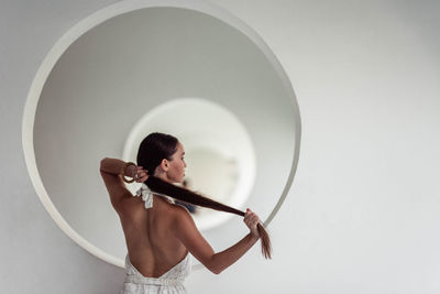 Tanned brunette with long hair stands against the background of white circles