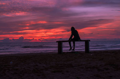 Silhouette man sitting on chair at beach during sunset