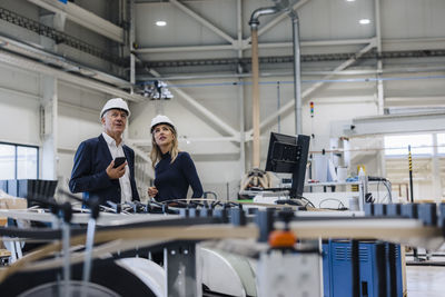 Businessman and colleague standing near machine in factory