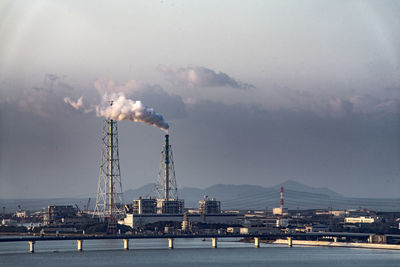 Smoke emitting from industry by sea against sky