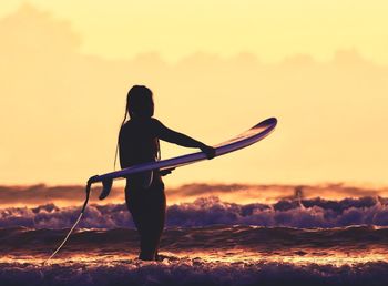 Silhouette woman with surfboard in sea against sky during sunset