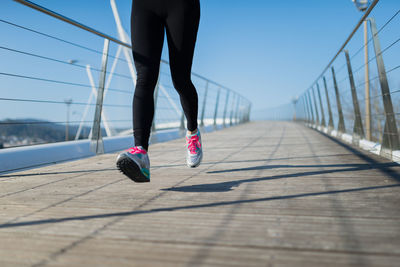 Low section of woman jogging on footbridge against clear sky