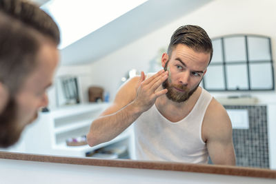 Young man applying facial cream while looking into mirror at home