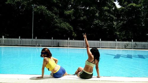 Rear view of female friends sitting at poolside