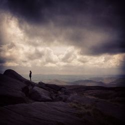 Rear view of woman standing on landscape against cloudy sky