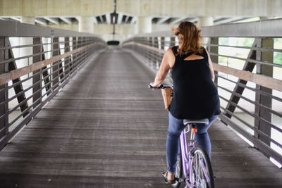 Rear view of woman riding bicycle on bridge