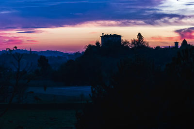 Silhouette trees and buildings against sky at sunset