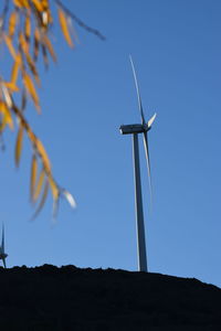 Low angle view of windmill on hill against clear sky