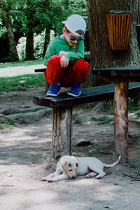 Boy looking at dog while crouching on bench in park