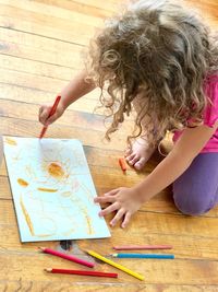 High angle view of girl drawing while crouching on hardwood floor