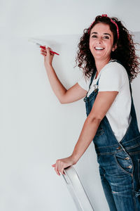 Portrait of smiling young woman standing against wall