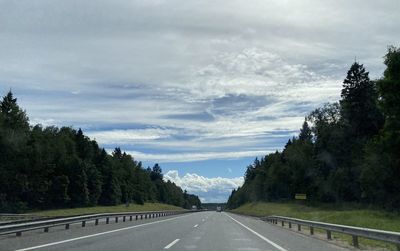 Empty road along trees and against sky