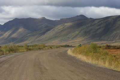 Dirt road amidst mountains against sky