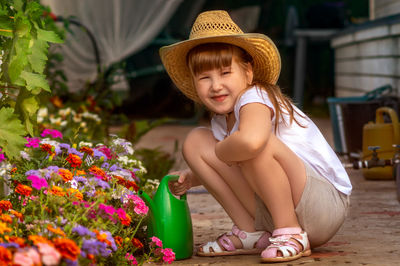 Lovely smiling little girl in straw cowboy hat outdoor in garden takes care of flower bed.