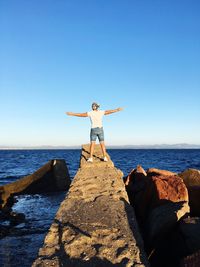 Man standing on rock by sea against sky