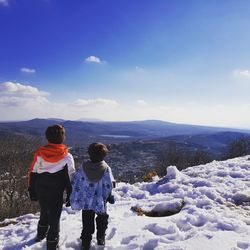 Rear view of children standing on snow covered mountain against sky