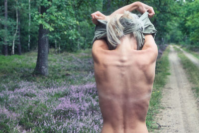 Rear view of shirtless naked woman removing t-shirt while standing on land