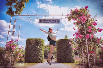 Young woman standing by flower tree against sky