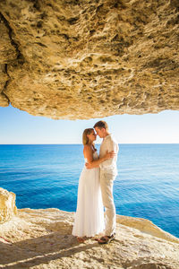 Full length of happy woman standing on rock by sea