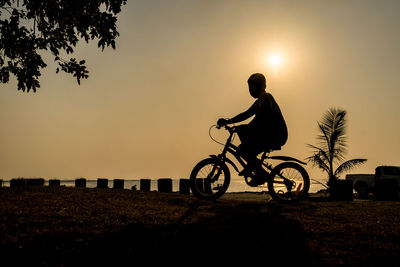 Silhouette man riding bicycle on field against sky during sunset