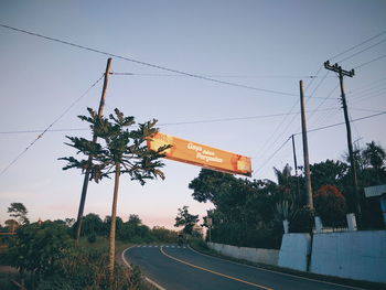 Road by trees against sky during sunset