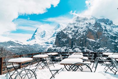 Chairs and tables on snow covered mountain against sky