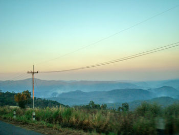 Electricity pylons against sky during sunset