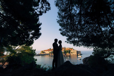 Man and woman standing by lake against sky