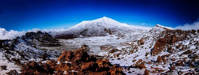 Scenic view of snow covered mountains against blue sky