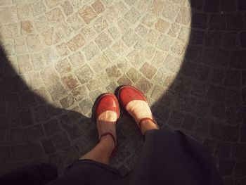 Low section of woman standing by sunlight on footpath