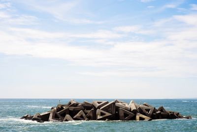 Groynes amidst sea against cloudy sky