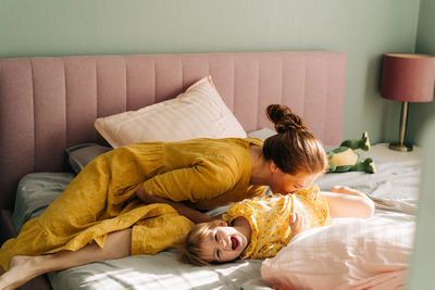 Mom and little daughter play and fool around on the bed.