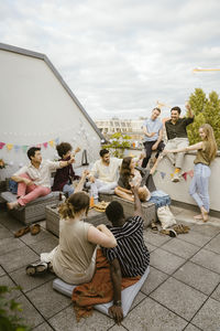 Happy male and female multiracial friends toasting drinks during party at rooftop deck