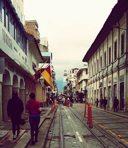 People walking on railroad track in city against clear sky