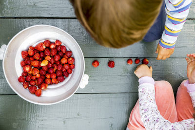 Overhead view of siblings playing with fresh harvested strawberries on floorboard