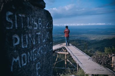 Rear view of man standing by sign against sky