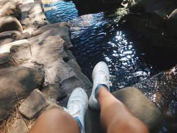 Low section of woman sitting on rock by river