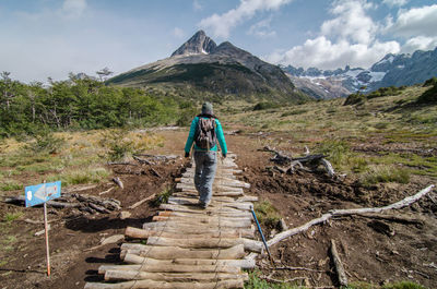 Rear view of mature woman with backpack walking on mountain against sky