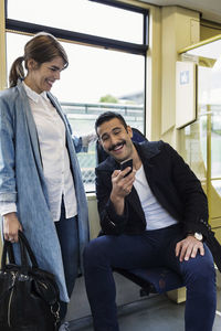 Happy young man showing mobile phone to woman in tram