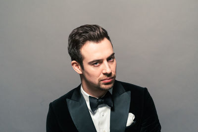 Portrait of arrogant young man wearing tuxedo against gray background