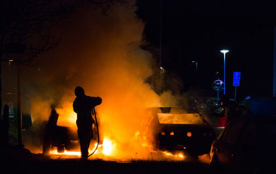 Rear view of firefighter extinguishing fire at night