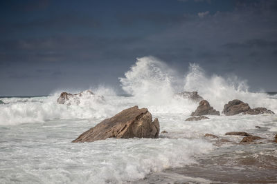 Waves splashing on rocks at shore against sky