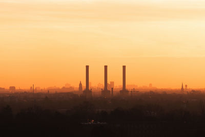 Silhouette factories in city against sky during sunset