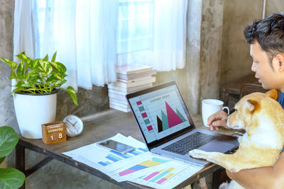 Man sitting with dog while working on laptop