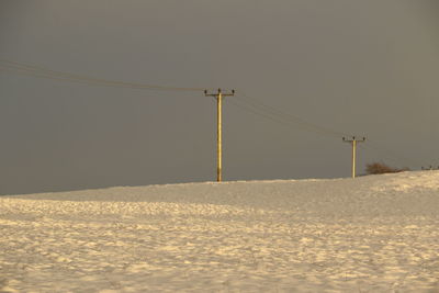 Electricity pylon on snow covered land against clear sky